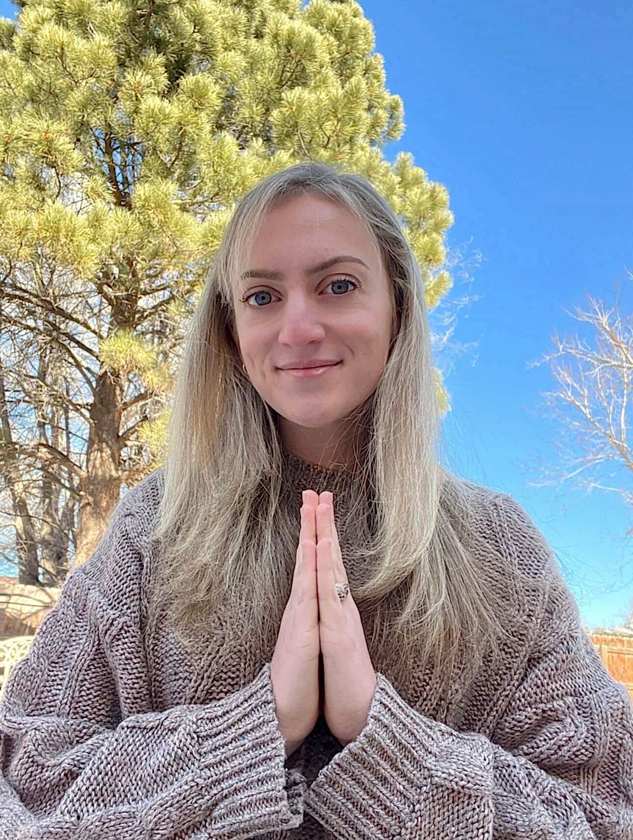 Photo of Sarah outside with a clear blue sky and her hands at hear center